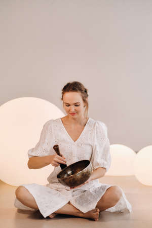 Portrait of a female yoga teacher playing a Tibetan bowl or singing a bell in the gym during a yoga...