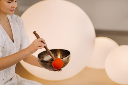 Portrait of a female yoga teacher playing a Tibetan bowl or singing a bell in the gym during a yoga retreat.の写真素材