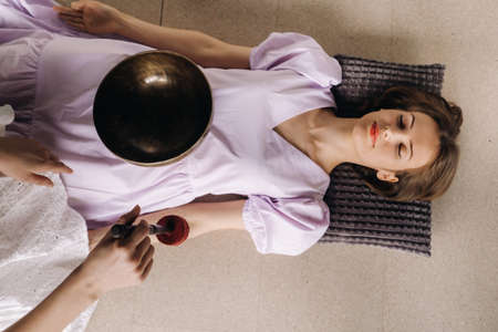 The copper singing bowl of the Nepalese Buddha in the spa. A young beautiful woman is doing a massage with singing bowls in a spa salon against the backdrop of a waterfall.の写真素材