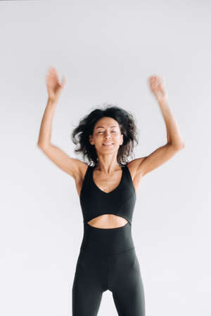A blurry silhouette of a woman in black sportswear jumps up and raises her arms up against a white background.の写真素材