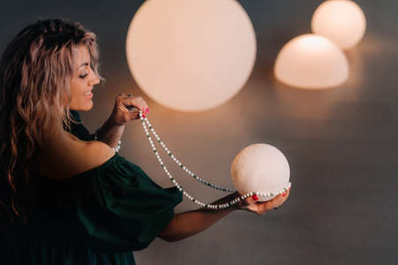 A girl in a green dress is sitting on the floor with a burning ball in her hands against a background of ballsの写真素材