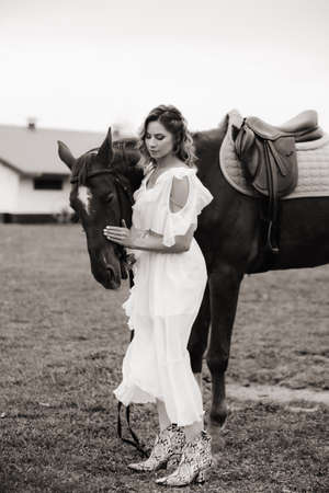Beautiful girl in a white sundress next to a horse on an old ranch. black and white photo.の写真素材