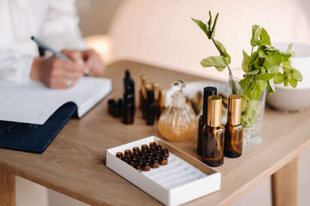 A close-up of bottles of essential oil and an aromatherapist writing a note in a notebook.の写真素材