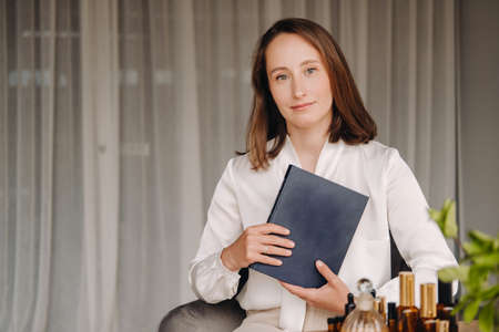 portrait of a smiling girl-woman sitting in an armchair. An aromatherapist in a white blouse is sitting in the office.