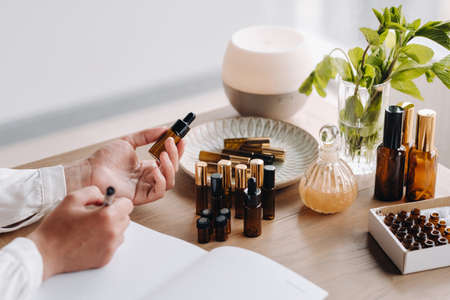 Close-up of female hands holding a bottle of essential oil and writing an entry in a notebook, aromatherapy.の写真素材