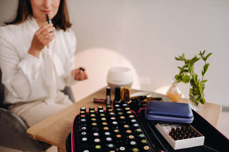 The aromatherapist girl is sitting in her office and holding a bottle of aromatic oils. there are essential oils on the table.の写真素材