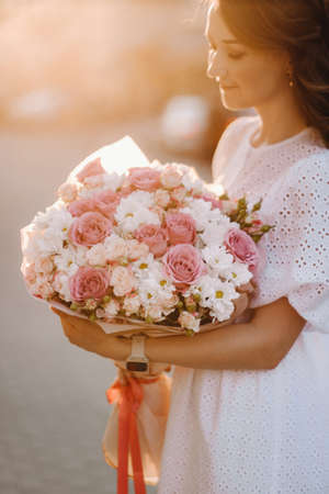A happy woman in a white dress at sunset with a bouquet of flowers in the city.の写真素材