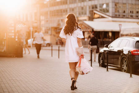 A happy woman in a white dress at sunset with a bouquet of flowers in the city.の写真素材