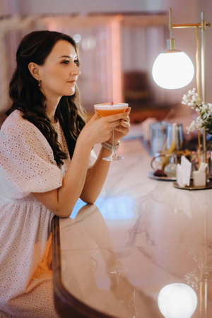 A girl in a white dress is sitting at the bar in a cafe and drinking a cocktail.の写真素材