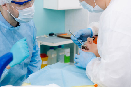A male dentist with dental tools drills the teeth of a patient with an assistant. The concept of...