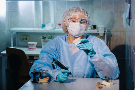 A dental technician in protective clothing is working on a prosthetic tooth in his laboratory.の写真素材