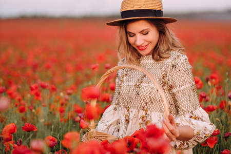 a girl in a dress with a hat and with a basket in a field with poppiesの写真素材