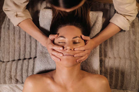 A cosmetologist girl does a facial and neck massage to a girl in the office for skin elasticityの写真素材