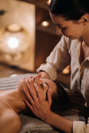 A cosmetologist girl does a facial and neck massage to a girl in the office for skin elasticity.の写真素材