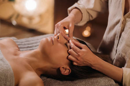 A cosmetologist girl does a facial and neck massage to a girl in the office for skin elasticity.の写真素材