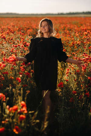 a girl in a black dress on a poppy field at sunset.の写真素材