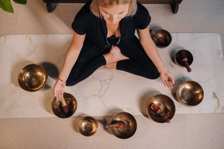 A woman sits in a lotus position next to Tibetan bowls, sitting on a yoga mat against the background of a gongの写真素材