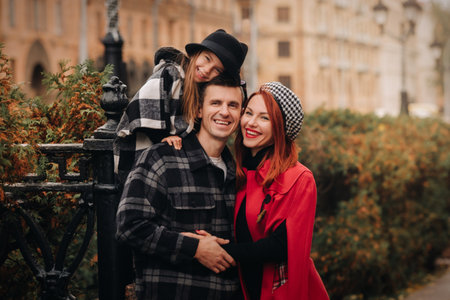 A stylish family of three strolls through the autumn city posing for a photographer . Dad, mom and...