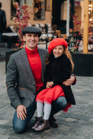 Portrait of a father and daughter sitting on a knee and being on a city street in autumnの写真素材