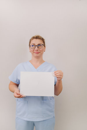 Portrait of a female doctor in a blue robe holding a white blank sheetの写真素材