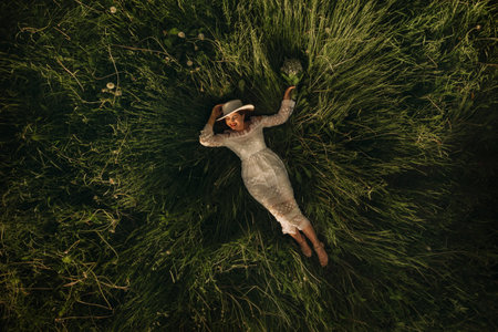 Portrait of a beautiful woman in a white dress and a hat with lilies of the valley. A girl in nature. Spring flowersの写真素材