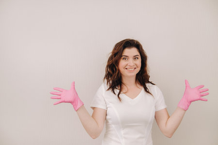 A smiling doctor in pink gloves and a white coat looks at the camera on a light backgroundの写真素材
