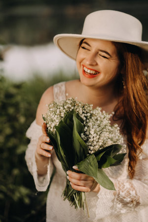 Portrait of a beautiful woman in a white dress and a hat with lilies of the valley. A girl in nature. Spring flowersの写真素材