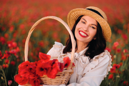 A girl in a white dress and with a basket of poppies walks through a poppy fieldの写真素材