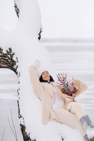 A beautiful girl in a beige cardigan and a white hat with flowers enjoys a snowy winter in natureの写真素材
