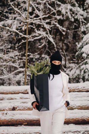 A girl in a white suit and balaclava with a package of Christmas trees in the winter forest on New Years Eve.New Years conceptの写真素材