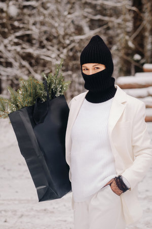 A girl in a white suit and balaclava with a package of Christmas trees in the winter forest on New Years Eve.New Years conceptの写真素材