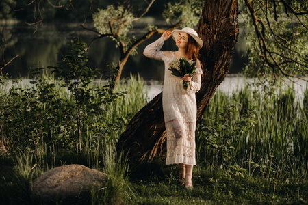 Portrait of a beautiful woman in a white dress and a hat with lilies of the valley. A girl in nature. Spring flowersの写真素材