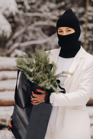 A girl in a white suit and balaclava with a package of Christmas trees in the winter forest on New Years Eve.New Years conceptの写真素材