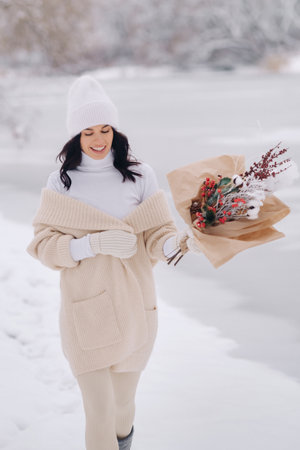 A girl in a beige cardigan and winter flowers walks in nature in the snowy season. Winter weatherの写真素材
