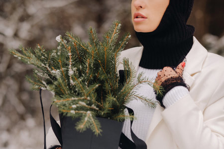 A girl in a white suit and balaclava with a package of Christmas trees in the winter forest on New Years Eve.New Years conceptの写真素材