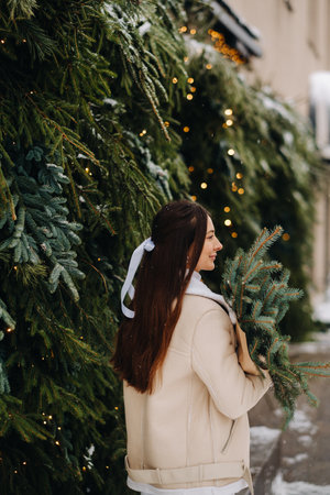 A girl with long hair stands with her back in a winter forest with a bouquet of fir branches. Snowy winterの写真素材