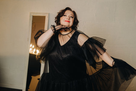 An elegant adult woman in a black cocktail dress poses in the interior. Fashionable portrait of a...