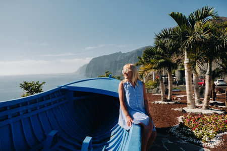 A girl sits on an observation deck against the backdrop of the Acantilados de Los Gigantes mountains...