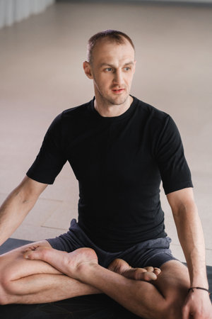 Portrait of an adult athletic man sitting in the lotus position in the gym on the mat.の写真素材