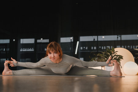 A girl in a gray sports uniform does yoga on a mat in the gym.