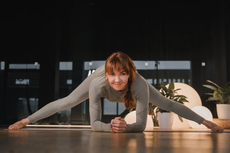 A girl in a gray sports uniform does yoga on a mat in the gym.