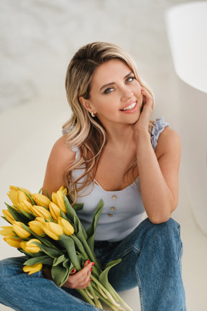 Cute smiling girl with a bouquet of yellow tulips in the interior.の写真素材