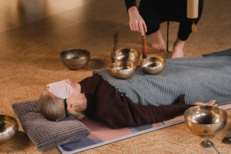 A young beautiful woman is doing a massage with singing bowls and a koshi bell to another girl. sound therapy.の写真素材