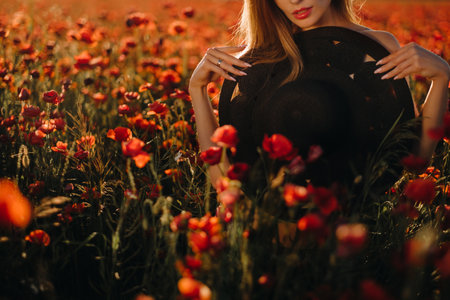 naked girl with a black hat in her hands in a poppy field at sunset.の写真素材