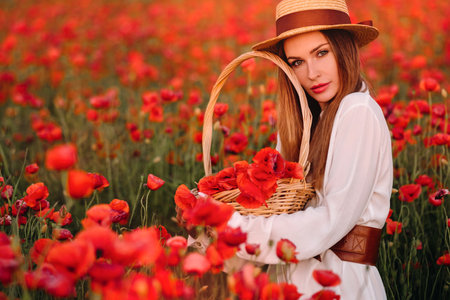 a girl in a white dress, a hat and with a basket in a field with poppies.の写真素材