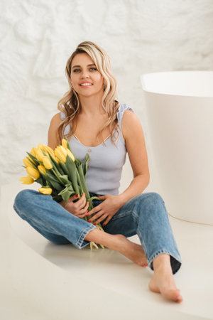 Cute smiling girl with a bouquet of yellow tulips in the interior.の写真素材