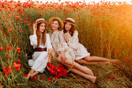 Funny girls in dresses and hats in a poppy field at sunset.の写真素材