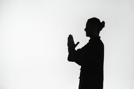Silhouette of a person practicing qigong energy exercises on a light background.の写真素材