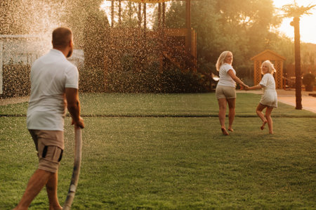 A man pours water from a hose on his wife and daughter on the lawn.の写真素材