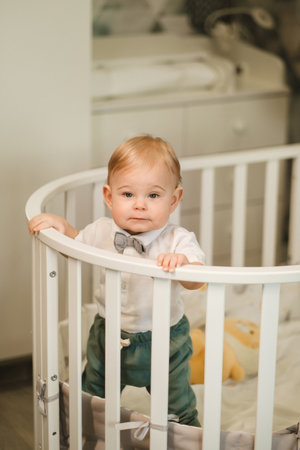 Portrait of a cheerful little boy in a white shirt with a bow tie standing in a crib.の写真素材